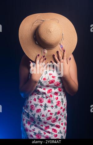 Belle femme debout portant une robe colorée avec un chapeau couvrant toute sa tête. Isolé sur fond fumé coloré. Banque D'Images