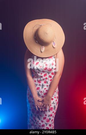 Belle femme debout portant une robe colorée avec un chapeau couvrant toute sa tête. Isolé sur fond fumé coloré. Banque D'Images