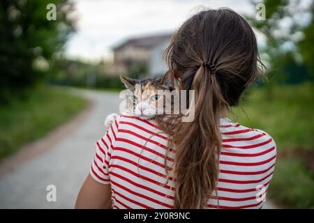 Vue arrière du dos de la femme, fille tenant un chat sérieux, visage jetant un coup d'œil sur l'épaule avec une expression dure Banque D'Images