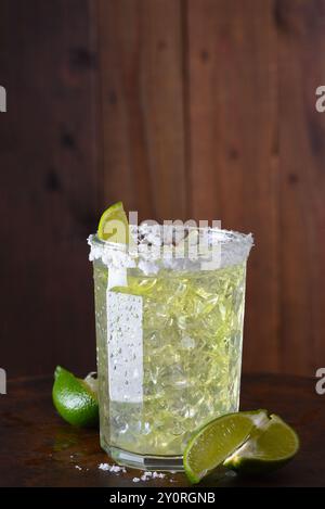 Une margarita sur les rochers dans un gobelet en verre. Le bord du verre est incrusté de sel et les limes tranchées sont sur la surface de la barre. Banque D'Images