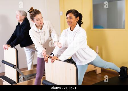 Femme hispanique pratiquant le pilates sur réformateur avec une jeune femme entraîneur Banque D'Images