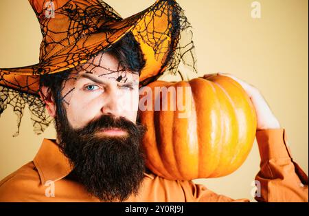 Ingrédients de cuisine de saison de Thanksgiving. Beau homme en chapeau d'Halloween tenant la citrouille - portrait gros plan. Jeune homme avec chapeau de sorcière prêt à Banque D'Images
