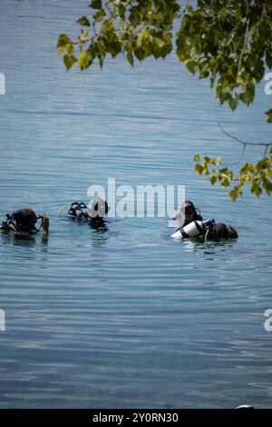 25 août 2024, Ohrid Bay of the Bones, Macédoine du Nord plongeurs en combinaisons noires de plongée sous-marine, un homme et une femme avec des bouteilles d'oxygène coulent sous le transp Banque D'Images