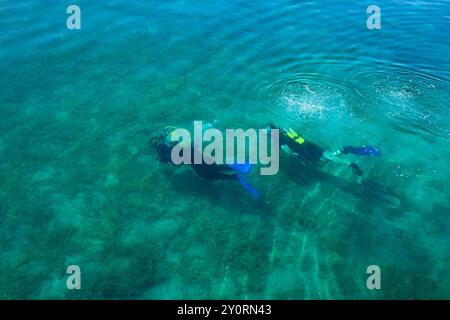 Plongeurs en combinaisons de plongée sous-marine noires, un homme et une femme avec des bouteilles d'oxygène coulent sous l'eau bleue transparente dans le lac Ohrid. Banque D'Images