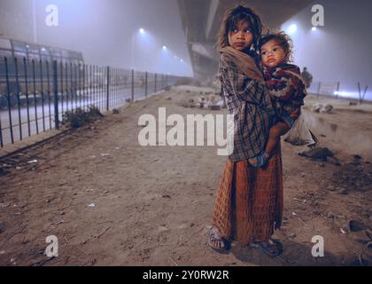 New Delhi, Inde, 21.01.2010, Une jeune fille sans abri tient sa sœur dans ses bras. Elle et sa famille cherchent un endroit pour dormir, Inde, Asie Banque D'Images