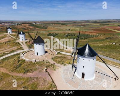 Quatre moulins à vent blancs avec des toits noirs sur une large colline sous un ciel bleu clair et entouré de champs, vue aérienne, Alcazar de San Juan, Ciudad Real, C. Banque D'Images