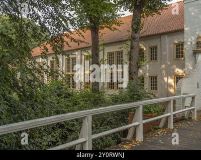 Bâtiment historique avec de grandes fenêtres et des tuiles rouges, entouré d'arbres, donnant sur un pont en bois blanc, dornum, frise orientale, allemagne Banque D'Images