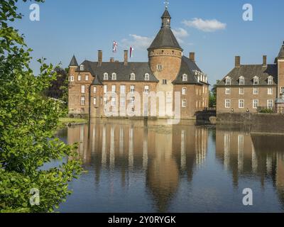 Un château à douves de briques avec des tours et des drapeaux, reflété dans l'étang et entouré de plantes vertes et d'arbres, Anholt, Rhénanie du Nord-Westphalie, Allemagne, Banque D'Images