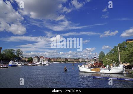 Vue d'un port plein de navires sous un ciel bleu avec des nuages et un panorama de la ville sur l'eau, îles, Stockholm, Suède, Europe Banque D'Images