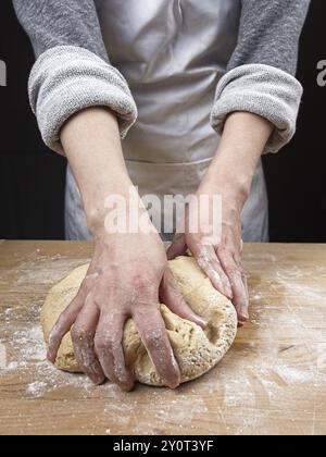 Une photo en gros plan des mains d'une femme pétrissant une grosse boule de pâte sur une planche à découper en bois Banque D'Images