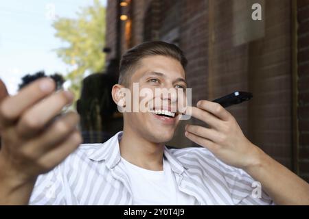 Jeune homme enregistrant des messages vocaux via smartphone à l'extérieur Banque D'Images