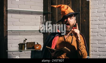 Homme face effrayant avec l'horreur maquillage tenant la tête de citrouille lanterne jack sur fond de ciel. Sorcellerie mal avec cheveux rouges et barbe dans un manteau noir de lecture Banque D'Images
