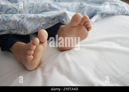 Les pieds d'une petite fille peuvent être vus jeter un coup d'œil par dessous une couverture confortable sur un lit Banque D'Images