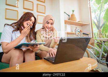 Deux indonésiennes sont assises sur un canapé regardant un ordinateur portable. L'un d'eux porte un foulard Banque D'Images