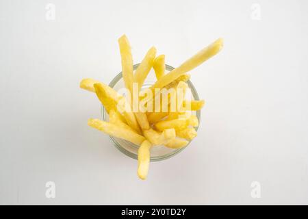 Un bol de frites est montré dans un verre. Les frites sont coupées en longs morceaux et empilées dans le bol. Le bol est placé sur un fond blanc, Banque D'Images