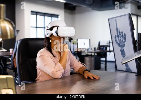 En utilisant un casque VR, femme explorant la conception robotique de main sur ordinateur dans le bureau Banque D'Images