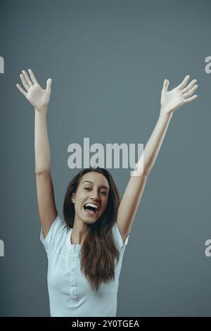 Jeune femme lève les bras dans l'excitation avec un grand sourire sur son visage. Elle est ravie de quelque chose et veut exprimer sa joie Banque D'Images