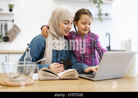 Mère musulmane et fille magasinant en ligne pour cuisiner des ingrédients à l'aide d'un ordinateur portable Banque D'Images