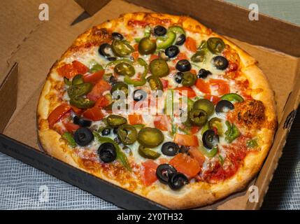 Pizza végétarienne. Olives noires, poivrons verts, tomate et garniture jalapeño dans une boîte à emporter. Banque D'Images