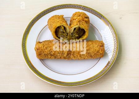 Savoureux rouleau de printemps de poulet entier et un rouleau de poulet coupé en deux sur une assiette sur fond de bois. C'est une collation populaire au Bangladesh. Banque D'Images