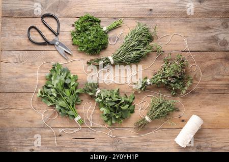 Bouquets de différentes herbes aromatiques, bobine de fil et ciseaux sur table en bois, pose à plat Banque D'Images