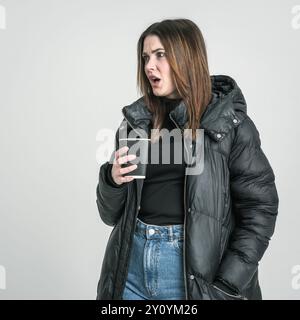 Femme tenant une tasse de café l'air choquée Banque D'Images