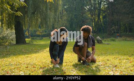 Deux personnes femme homme coureurs sportifs fille gars Indien couple arabe debout dans le parc à l'extérieur forêt parlant amical parler parler parler nouant sneakers Banque D'Images