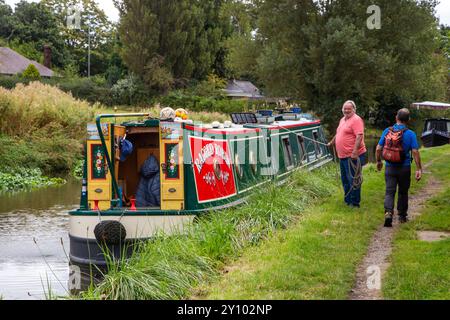 Homme marchant le long du chemin de halage du canal Trent et Mersey devant un homme amarrant son bateau étroit pour la journée dans la campagne du Cheshire près d'Anderton Banque D'Images