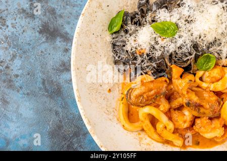 Fruits de mer Ink pâtes aux nouilles de seiche avec des anneaux de calmars et de moules sous parmesan. Restaurant servant sur un fond bleu Banque D'Images