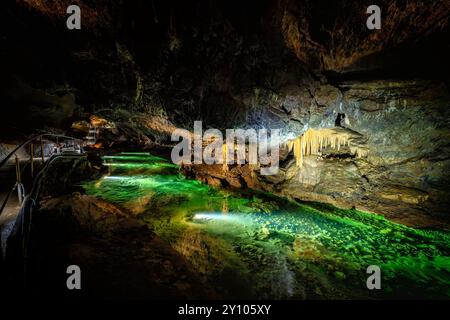 Grotte souterraine illuminée avec eau verte incandescente, stalactites et formations rocheuses. Un paysage souterrain magique avec des reflets. Banque D'Images