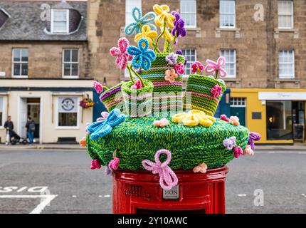 Topper tricoté de pots de fleurs colorés sur la boîte aux lettres rouge Royal mail, Haddington High Street, Écosse, Royaume-Uni Banque D'Images