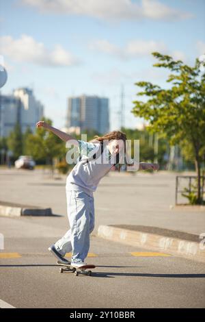 Plan vertical d'un adolescent dreadlocked cool avec un sac à dos skateboard dans une rue ensoleillée de la ville à l'école en équilibre à bord, espace copie Banque D'Images