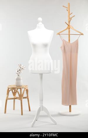 Un mannequin féminin sur le stand, rack avec robe, tabouret et fleurs de coton dans un vase sur fond clair Banque D'Images