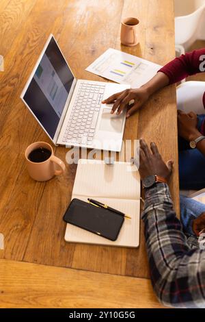 Collaborer à la maison, couple afro-américain utilisant un ordinateur portable et examinant des documents avec des tasses à café Banque D'Images