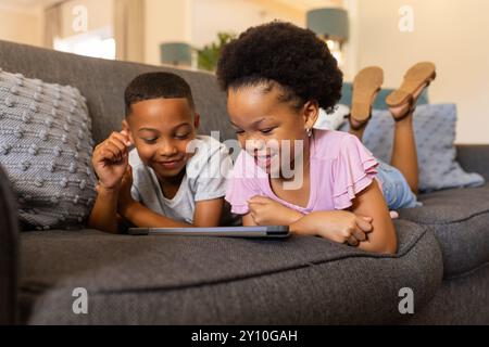frère et sœur allongés sur le canapé, regardant la tablette et souriant, profitant du temps ensemble Banque D'Images
