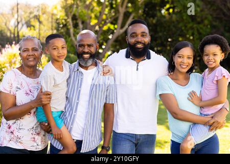 Debout ensemble et souriant, famille multi-générationnelle dans le jardin ensoleillé en plein air Banque D'Images