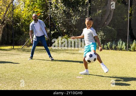 Jouer au football, petit-fils donnant un coup de pied au ballon tout en regardant grand-père sur le terrain extérieur Banque D'Images