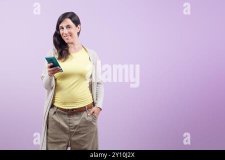 Une femme tient un téléphone portable dans sa main. Elle sourit et regarde la caméra Banque D'Images