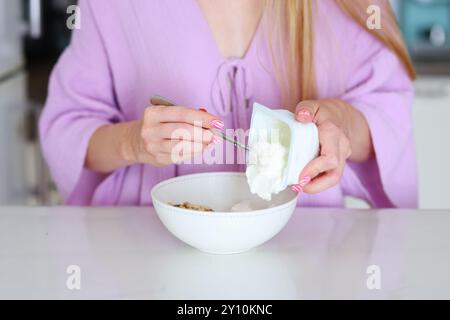 mains féminines mettant du yaourt avec un concept de petit déjeuner sain au muesli Banque D'Images