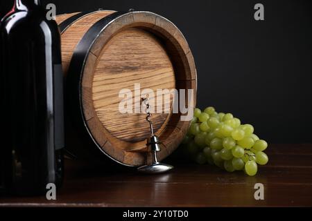 Tire-bouchon avec poignée en métal, raisins, bouteille de vin et tonneau sur table en bois Banque D'Images