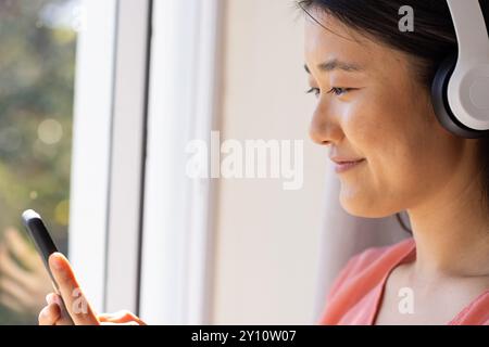 Écouter de la musique sur des écouteurs, femme asiatique souriante et utilisant un smartphone Banque D'Images
