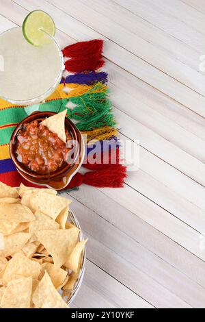 Vue aérienne d'un cocktail de margarita avec frites et salsa sur une table en bois rustique blanc. Format vertical avec espace de copie. Banque D'Images