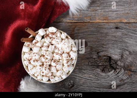 Plan à angle élevé d'une grande tasse de cacao chaud avec des guimauves sur une table en bois rustique à côté d'un chapeau de Père Noël. Banque D'Images