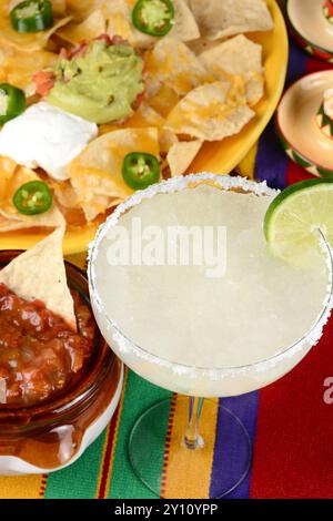 Vue en haut angle d'un cocktail de margarita entouré de nachos, frites, salsa sur un mexicain lumineux, nappe. Format vertical. Parfait pour Cinco de May Banque D'Images