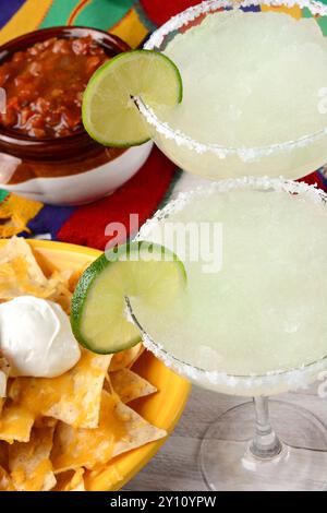 Vue panoramique de deux cocktails à la margarita pour une célébration du Cinco de Mayo. Entouré de croustilles de nacho et de salsa sur une nappe mexicaine brillante. Banque D'Images