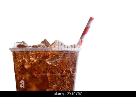 Gros plan d'une tasse en plastique remplie de glace et de cola. Seule la moitié de la tasse est représentée avec une paille rayée rouge et blanche sur un fond blanc. Banque D'Images