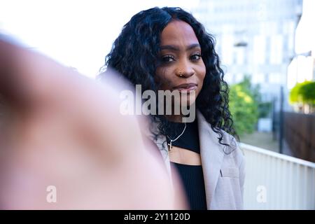 Jeune femme ayant un appel vidéo avec un téléphone portable et souriant à l'extérieur. Banque D'Images