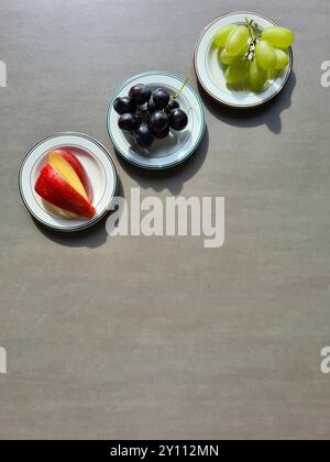 Fruits frais sur une assiette blanche, un régime riche en vitamines, raisins frais sains légers et foncés et pommes rouges tranchées Banque D'Images