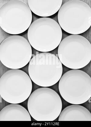 Assiettes blanches vides disposées les unes à côté des autres comme un motif et photographiées d'en haut comme une image en noir et blanc Banque D'Images