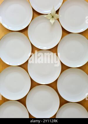 Des assiettes blanches vides se tiennent côte à côte sur une table en bois, une fleur de cornouiller blanche est disposée entre les assiettes comme décoration Banque D'Images